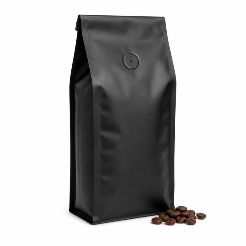 Matte black flat-bottom coffee pouch with a round degassing valve beside coffee beans